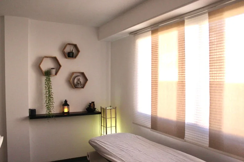 Sala de masaje con la camilla preparada, estanterías hexagonales de madera y luz natural filtrada